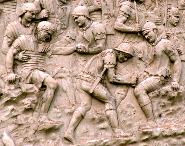 A detailed stone carving showing several injured Roman soliders being given medical assistance and others Roman soldiers standing in the background