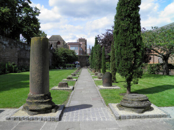 A central blockwork path lined either side by ruined pillars, mostly only a few inches high, and adjacent lawned areas with a variety of borders