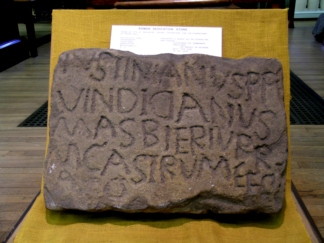 A colour photo showing a slightly irregular carved stone with four lines of Latin text that also seem to be slightly amateur in their presentation