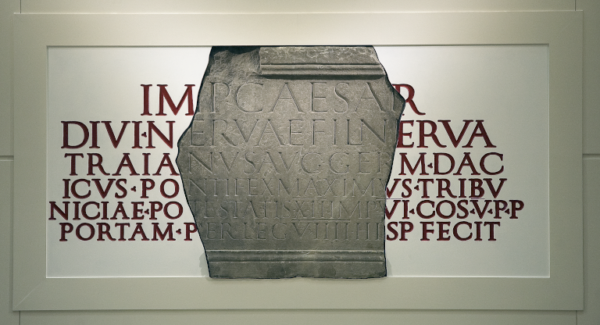 A colour photo showing a fragment of a carved stone inscription - this is set onto a reconstruction of the stone's full text, so that it can be read in its entirety