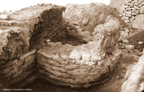 A black and white photo from Skelton in Cleveland in History - it shows extansive stone structures, mainly footings of a bastion, with adjoining defensive wall - there is some loose stone, in the background, probably from excavated of this site