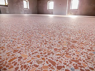 A colour photo showing a example of an opus signinum cast floor, made up of a mixture of broken tiles and mortar making it appear like solid stone - this example uses lots of pieces of terracotta tile