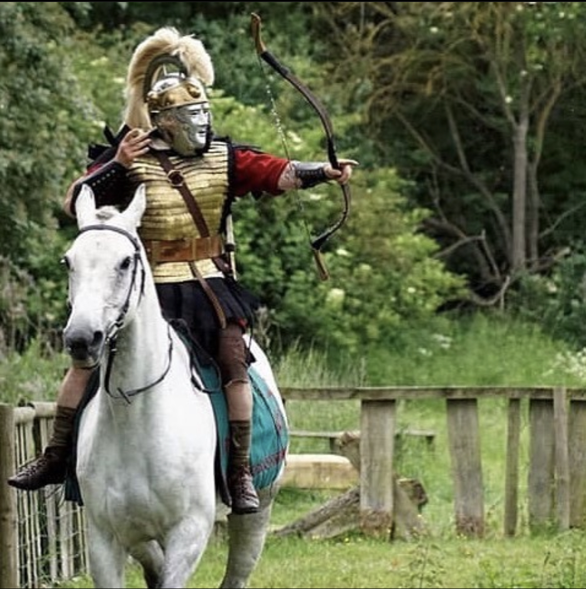 A photo of a Roman archer riding on a white horse whilst firing an arrow