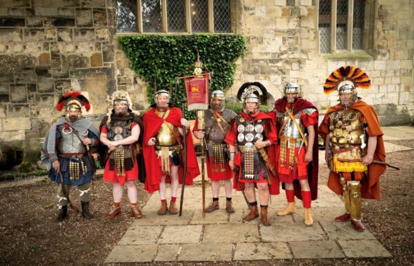 A group of 7 Roman soldiers dressed for battle, and posing in front of a stone building