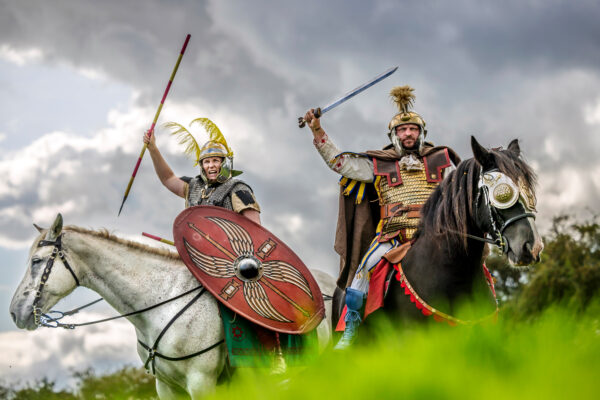 A colour photo showing two mounted cavalry riders, one on a white horse, the other on a black horse - both riders are raising their weapons ready to charge