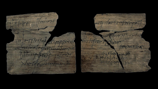 A fragmented wooden tablet with cursive Latin text inscribed in ink. The message is a birthday invitation.