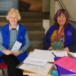 Two female volunteers seated at the entrance to a museum, both smiling.