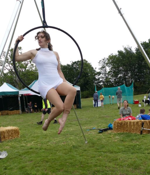 A woman in a white leotard swings from a hoop.