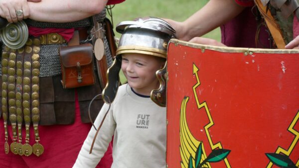 Child wearing a Roman helmet stands between two reenactors