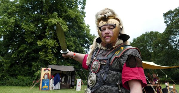 Man holding a sword stands dressed as Roman soldier with animal skin on head