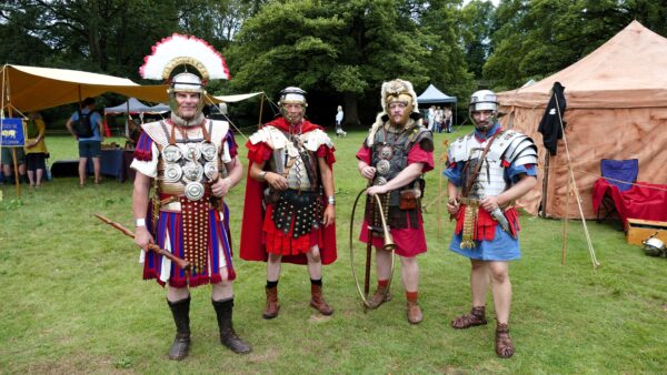 Four men dressed as ancient Roman soldiers stand in a field